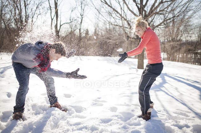 Pareja joven teniendo pelea de bolas de nieve en el parque de invierno - foto de stock