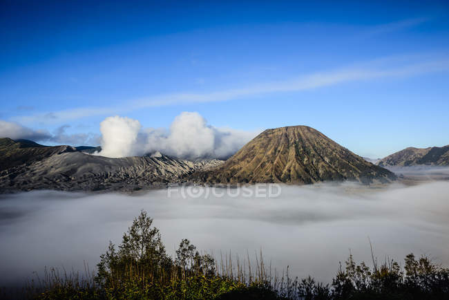 Vista de alto ángulo de las nubes bajo el volcán humeante - foto de stock