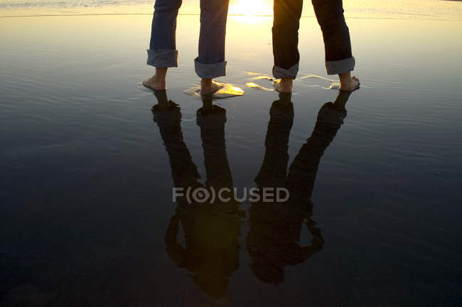 Reflection of couple legs in water at beach — Stock Photo