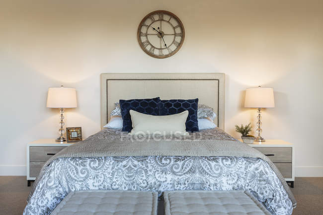 Bed and lamps in ornate bedroom with vintage clock on wall — Stock Photo