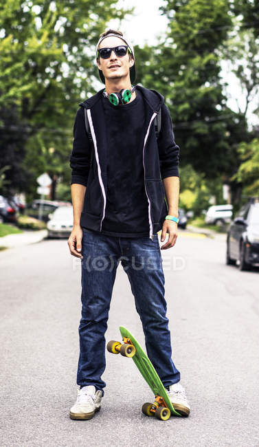 Белый мужчина в наушниках, стоящий на скейтборде — стоковое фото