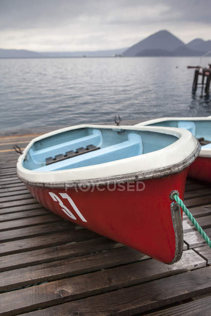 Red boats on wooden dock with mountains in distance — Stock Photo