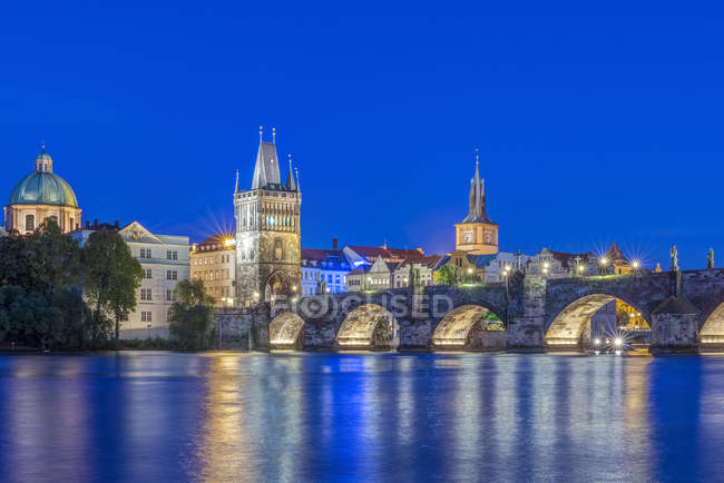 Charles Bridge and city illuminated at dusk, Prague, Czech Republic — Stock Photo