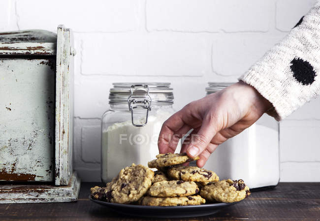Мужская рука берет печенье из тарелки с винтажными банками на столе — стоковое фото