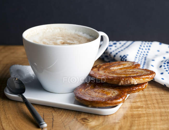 Nahaufnahme von Palmier-Keksen und Tasse Kaffee auf Porzellanteller — Stockfoto