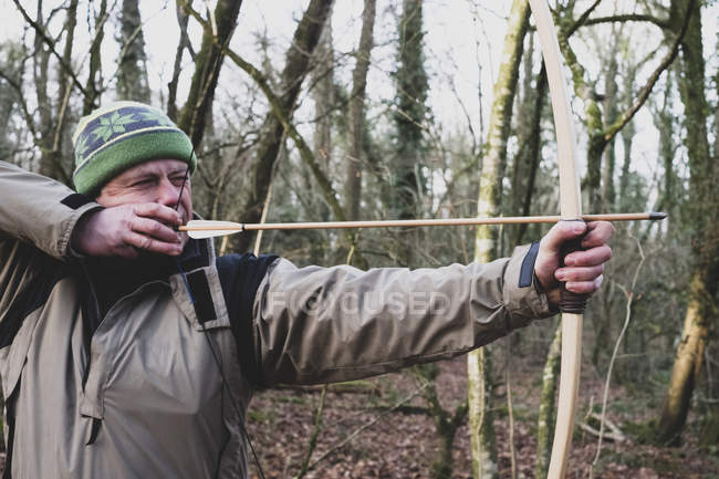 Primer plano del hombre de pie en el bosque y usando arco y flecha
. - foto de stock