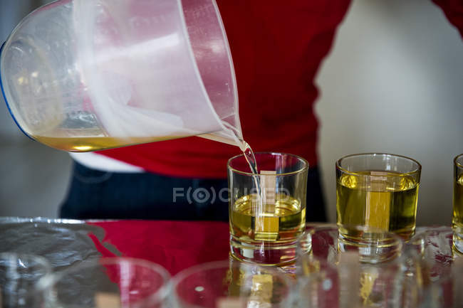 Close-up de pessoa derramando cera líquida para velas artesanais em frascos de vidro . — Fotografia de Stock