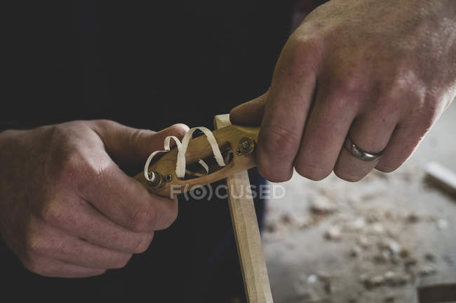 High angle close-up of man using plane on piece of wood. — Stock Photo