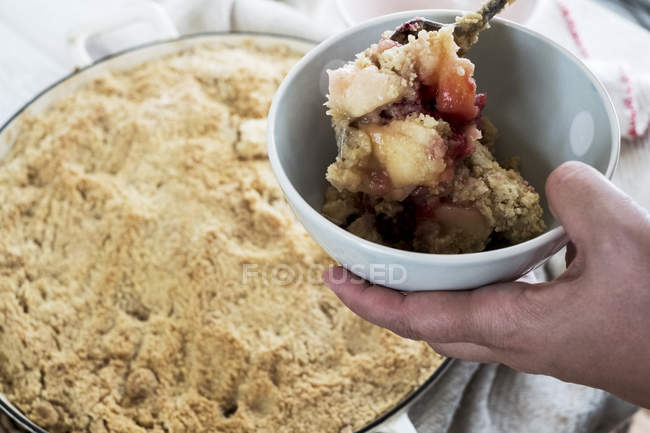 Close-up of person holding bowl of freshly baked apple and blueberry crumble. — Stock Photo