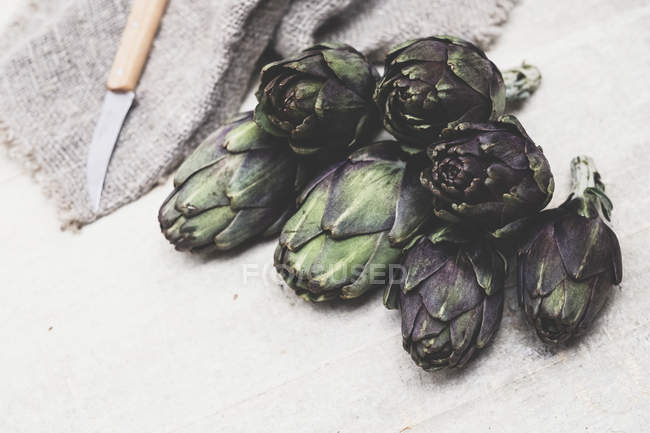 High angle view of kitchen knife and fresh artichokes on grey background. — Stock Photo