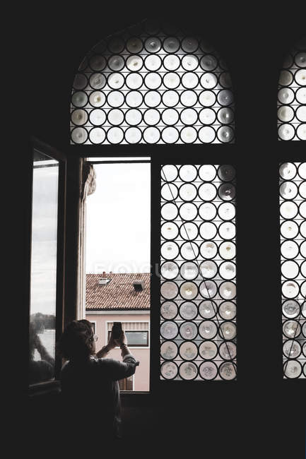 Vue arrière de la femme prenant une photo à travers une fenêtre cintrée avec du verre au plomb à Venise, Vénétie, Italie . — Photo de stock