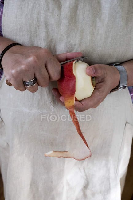 Nahaufnahme einer Frau, die einen roten Apfel mit einem doppelschneidigen Schäler schält. — Stockfoto