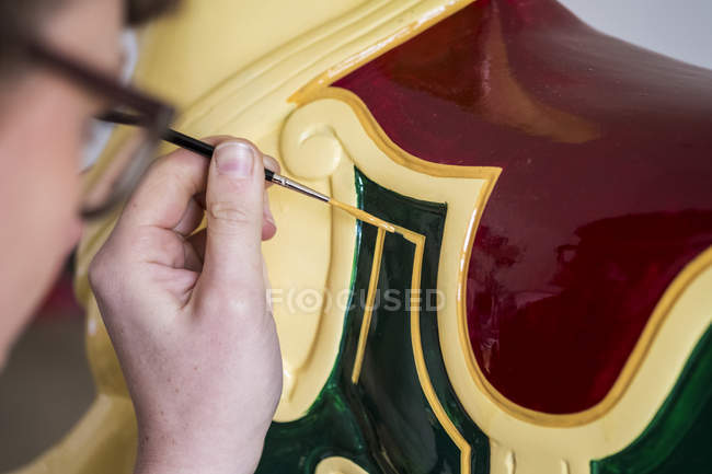 Gros plan de la femme dans des lunettes en atelier peignant le cheval traditionnel en bois du manège . — Photo de stock