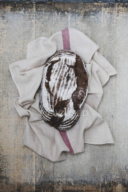 Top view of freshly baked loaf of brown bread on tea towel. — Stock Photo