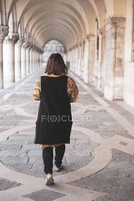 Вид сзади на женщину, идущую вдоль колоннады в Венеции, Венеция, Италия . — стоковое фото
