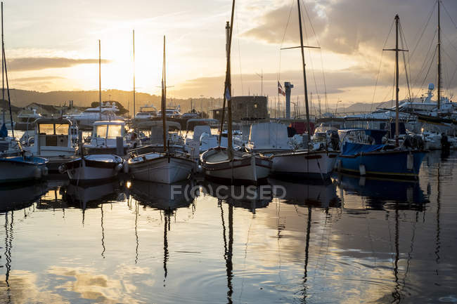 Sailboats moored in harbour reflecting in calm sea water at sunset. — Stock Photo