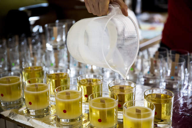 Primo piano di persona che versa cera liquida per candele fatte a mano in vasi di vetro . — Foto stock