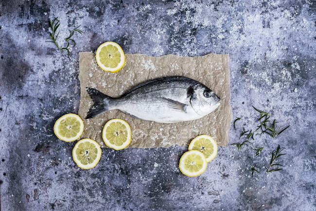 Vista dall'alto del pesce orata fresco decorato con fette di limone e rosmarino fresco . — Foto stock