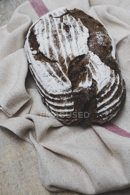 Крупный план свежеиспеченного буханки коричневого хлеба на чайном полотенце
. — стоковое фото