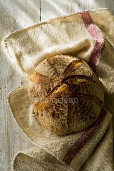 High angle close-up of freshly baked round loaf of bread on tea towel. — Stock Photo
