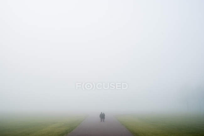 Two people walking along rural road on misty weather. — Stock Photo