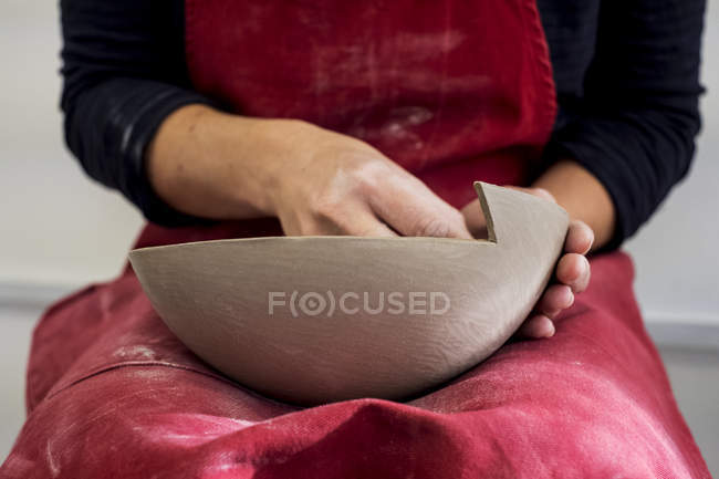 Midsection of ceramic artist in red apron working on small clay bowl. — Stock Photo