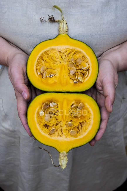 Close-up of person holding pumpkin with orange flesh cut in half. — Stock Photo