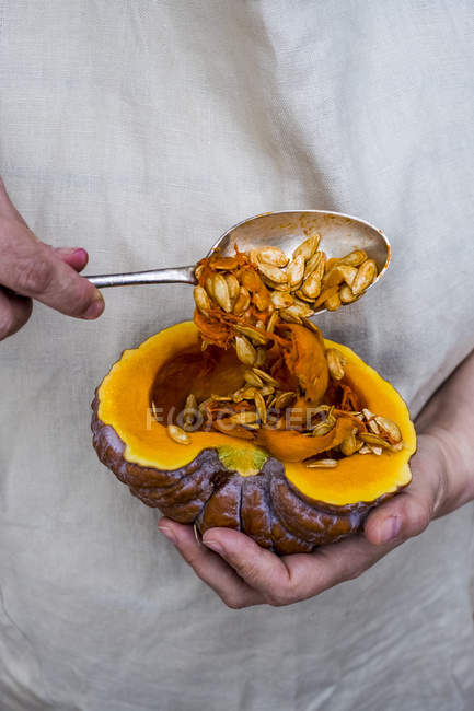 Close-up of person using silver tablespoon to removing seeds from cut pumpkin. — Stock Photo