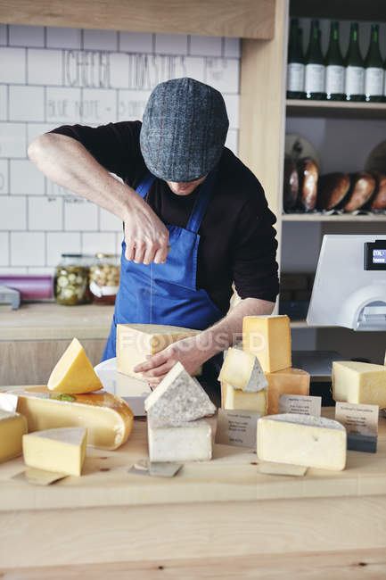 Cheesemonger cortar queso usando alambre de queso en la tienda - foto de stock