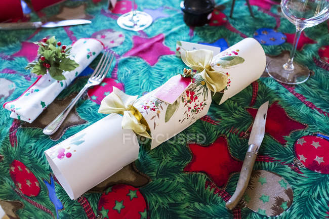Hochwinkel-Nahaufnahme von Besteck und weißem Weihnachts-Cracker auf grünem und rotem Tischtuch mit Weihnachtsmotiv. — Stockfoto