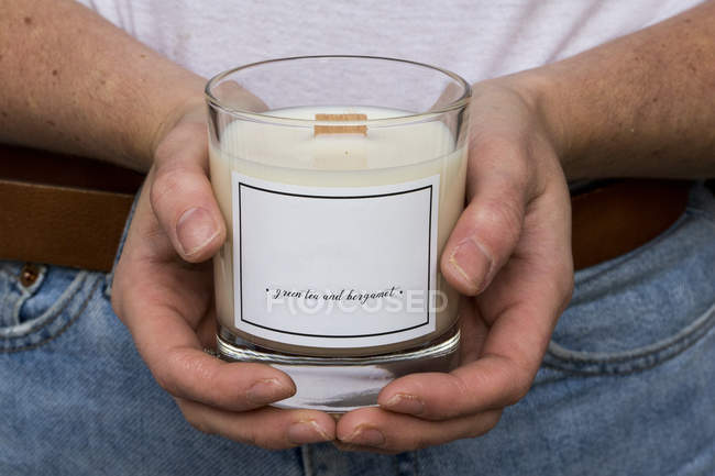 Close up of person holding handmade white and yellow jar candle with wooden wick. — Stock Photo