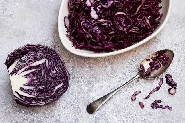Dish and spoon of sliced red cabbage and half of raw cabbage. — Stock Photo