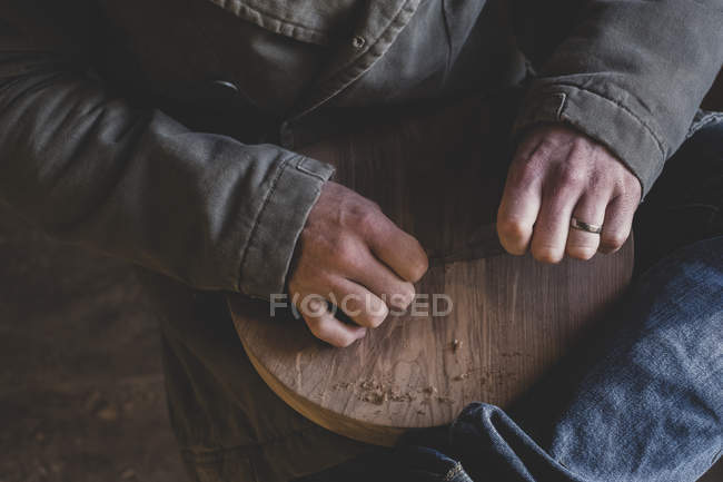 High angle close-up of man sitting in workshop, holding piece of wood. — Stock Photo