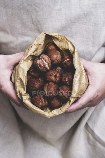 Закрыть лицо, держа коричневый бумажный пакет со свежими грецкими орехами . — стоковое фото