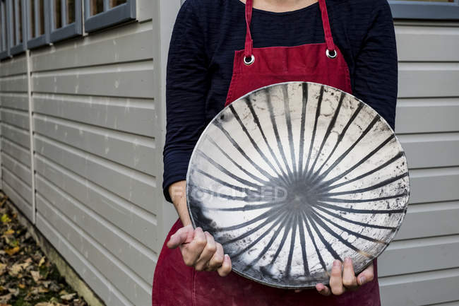 Midsection of woman in red apron holding ceramic bowl with black lines pattern. — Stock Photo