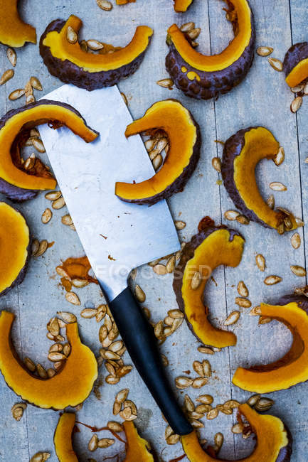 Close-up of cleaver and slices of pumpkin on blue background. — Stock Photo
