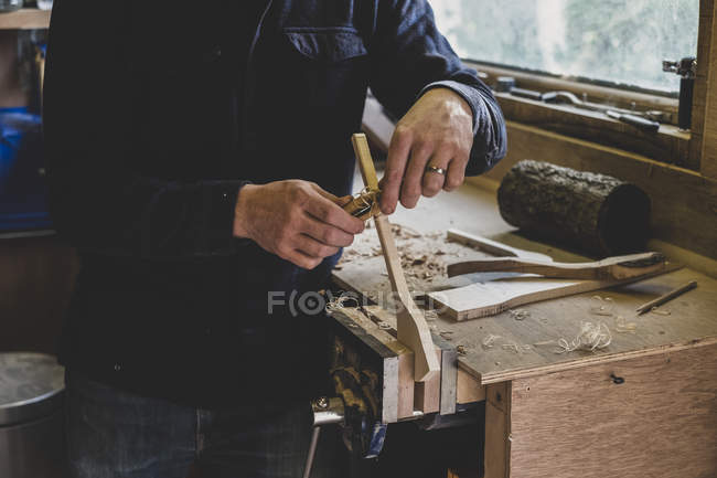 Mann steht an Werkbank in Werkstatt und bearbeitet Stück Holz. — Stockfoto