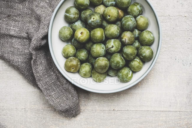 High angle close-up of fresh greengages in white bowl. — Stock Photo