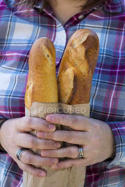 Nahaufnahme einer Person mit zwei frisch gebackenen französischen Baguettes in brauner Papiertüte. — Stockfoto