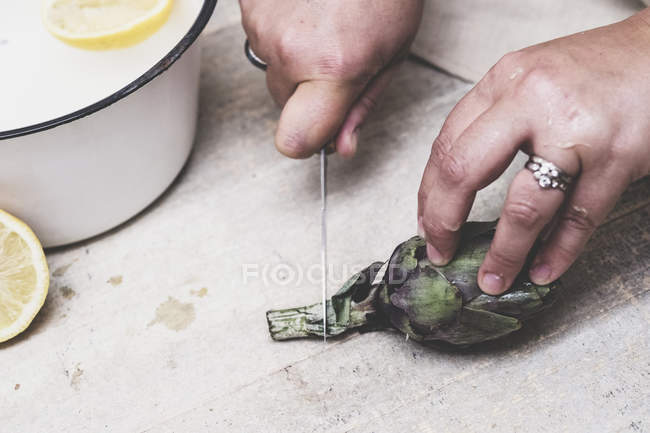 Close-up of person cutting fresh artichoke with kitchen knife. — Stock Photo