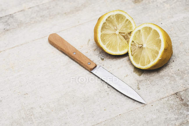 High angle close-up of kitchen knife and fresh lemon sliced in halves. — Stock Photo