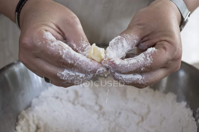 Close up of person rubbing in butter and flour for crumble between fingers. — Stock Photo