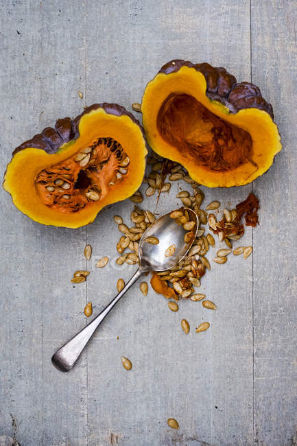 High angle view of silver tablespoon and purple pumpkin with orange flesh cut in half. — Stock Photo
