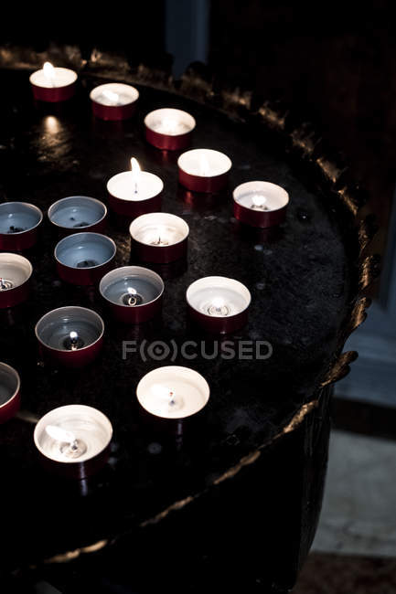 High angle close-up of lit tea light candles on tray in church. — Stock Photo