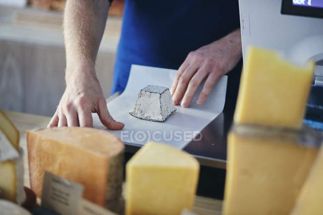 Cheeseseller wrapping up with hands goat cheese in store — Stock Photo