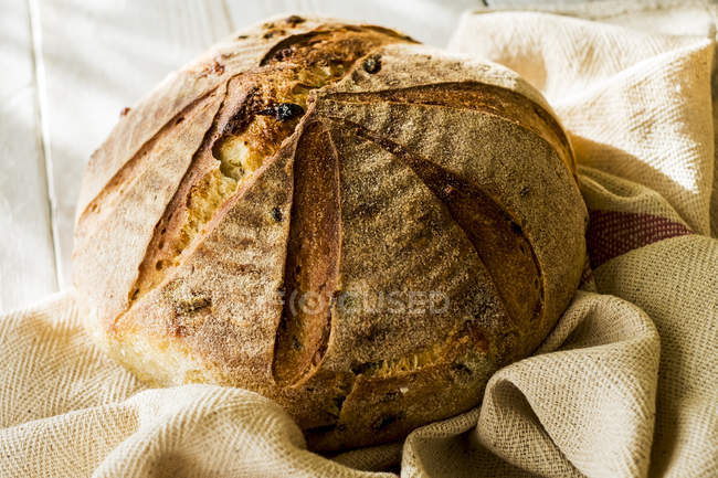 High angle close-up of freshly baked round loaf of bread on tea towel. — Stock Photo