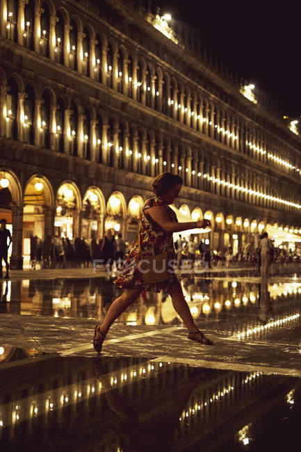 Женщина, перепрыгивающая через освещенную площадь Св. Марка в Венеции, Италия ночью . — стоковое фото