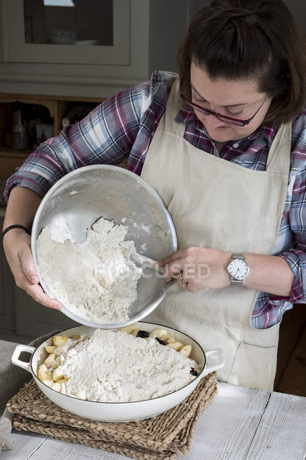 Mulher de avental em pé na cozinha, derramando mistura crumble fresco para torta prato — Fotografia de Stock
