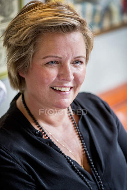 Portrait of smiling mature woman with short blonde hair in black blouse. — Stock Photo