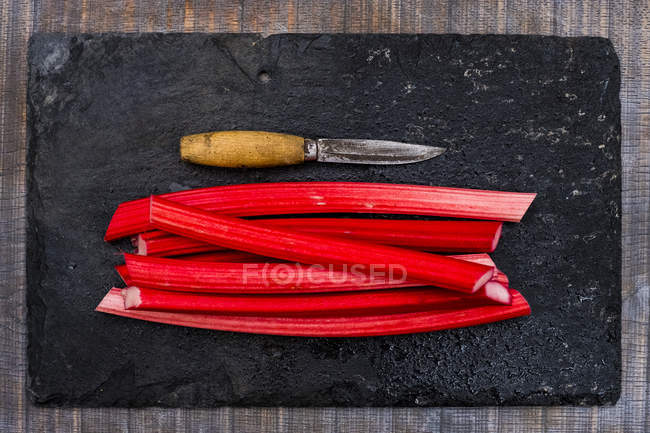 High angle close-up of rhubarb stalks and knife on black slate. — Stock Photo